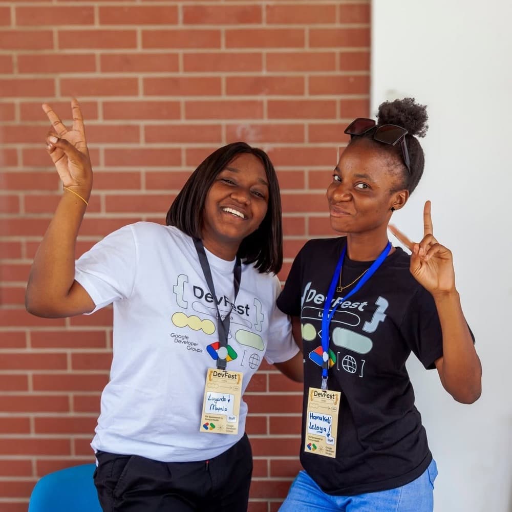 Two attendees in DevFest t-shirts and lanyards posing with peace signs